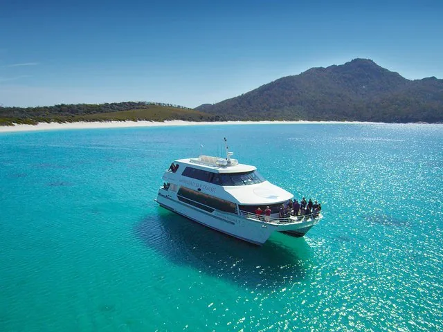 White cruise boat sailing in clear turquoise water near a sandy beach and hills