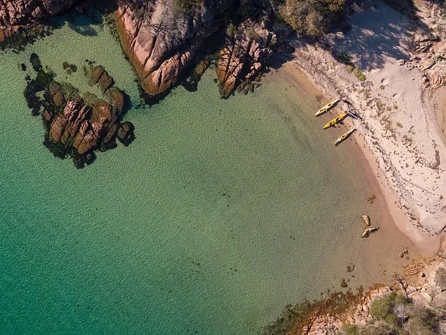 Aerial view of a sandy beach and clear green water with kayaks