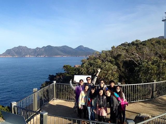 Group of tourists posing at a coastal lookout with a lighthouse.