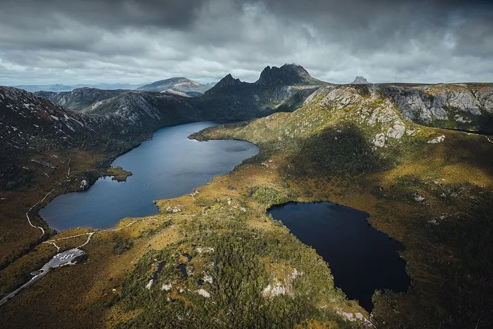 An aerial view of a lake nestled amongst mountainous terrain under cloudy skies.