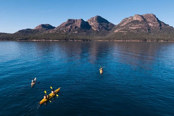 Three yellow kayaks paddling across deep blue water towards a mountain range