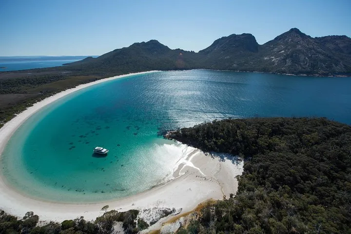 Aerial view of a boat in a curved bay with a white sand beach